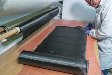 Specialist worker hands protected by gloves cutting carbon fiber.