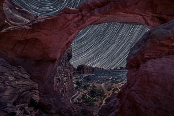 Star trails through Double Arch in Arches National Park, Utah during summer time with dark sky background, stars moving across the sky