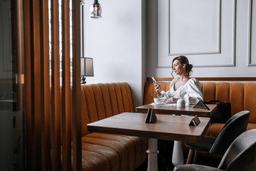 A young beautiful woman uses her smartphone for business, writes stories, takes selfies, blogs, and talks to friends in cafe