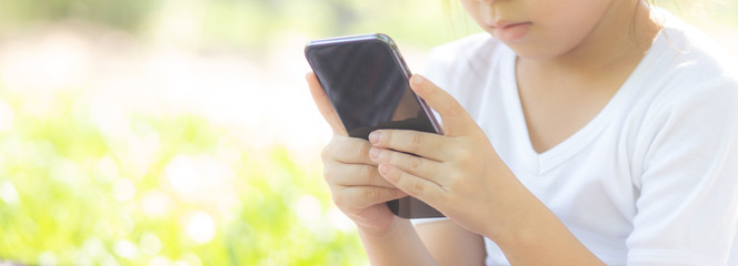Beautiful asian child smiling using smart mobile phone in the garden, kid playing game digital on smartphone on internet in the park with happy, lifestyle and technology concept, banner website.