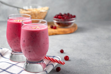 Two glasses with freshly homemade smoothie of yogurt, oatmeal and cranberries on a gray table. Healthy eating concept, image with copyspace