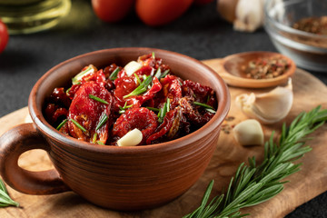 Sun-dried tomatoes with garlic, rosemary and spices in a clay bowl on an olive wood cutting board