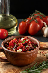 Sun-dried tomatoes with garlic, rosemary and spices in a clay bowl on an olive wood cutting board, vertical image
