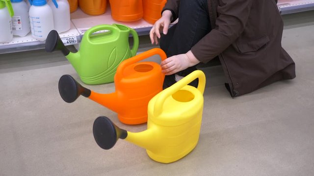 adult woman carefully chooses garden watering can in supermarket