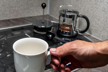 Close up over the shoulder angle of a person's hands fixing coffee in a black and stainless steal metal french press over a small stove covered in glass and grey counter top inside one early morning.