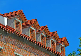 red brick tile roof with triangle windows line on blue sky in sunny day, construction diversity