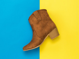 Brown suede stylish boot on a yellow and blue background.