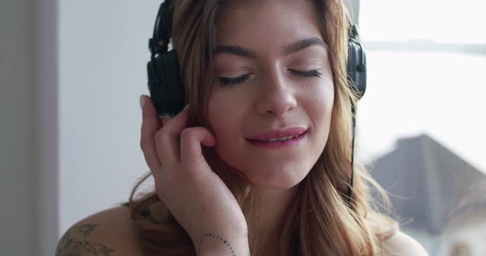 Woman with headphones, touches the earcups, dreams, gazes at camera and flirts