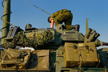 Soldier reaching into the gun turret of a green Canadian army light armoured vehicle