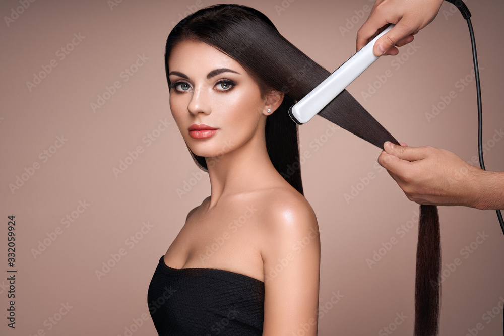 Wall mural hairdresser straightening long dark hair with hair irons. beautiful woman with long straight hair. s