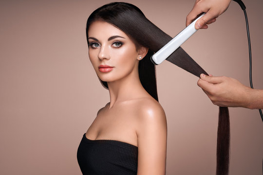 Hairdresser straightening long dark hair with hair irons. Beautiful woman with long straight hair. Smooth hairstyle