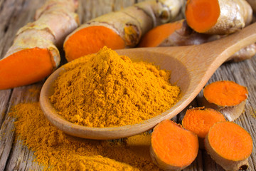 Turmeric powder and fresh turmeric (curcumin) on wooden background