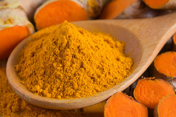 Turmeric powder and fresh turmeric (curcumin) on wooden background.