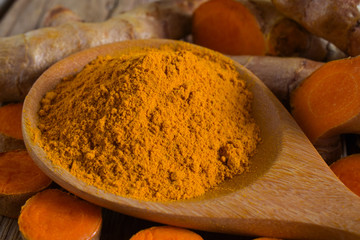 Turmeric powder in a wooden ladle and turmeric (curcumin) rhizome on a wooden background.