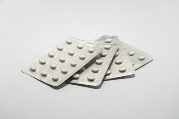 Foil packets of white tablet pills medication on plain white background. Cure and treatment concept.