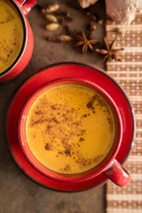 Red cup of golden milk with turmeric powder and cinnamon on a dark background. Close-up. A healthy drink to enhance immunity. Healthy drink. Super food