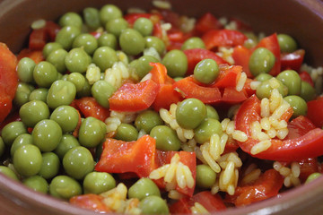 A vegetarian dish of rice, green peas, red bell pepper and tomato in a clay pot as a symbol of healthy eating.
