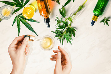 Pipette with CBD cosmetic oil in female hands on a table background with various bottles with...