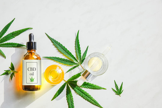 Glass brown bottle with cannabis CBD oil with label and marijuana leaves on a marble background. Copy space