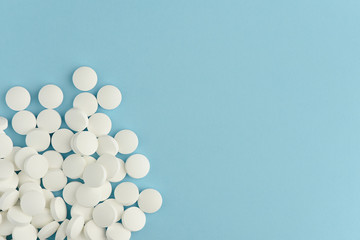 White round pills scattered on blue background. Medicine flat lay with copy space. 