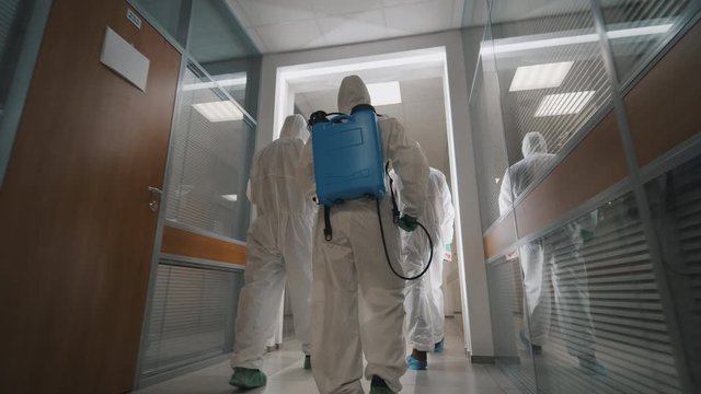 Team of specialists in hazmat suits with disinfection equipment in office center
