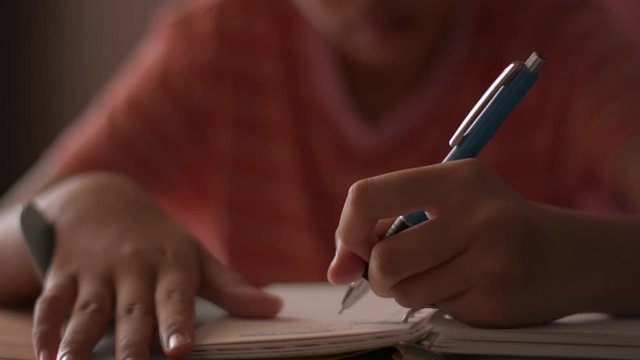 Close up hand of a little girl writing on notebook. Female schoolchild making notes on a diary. Doing homework with writing material. Education concept.