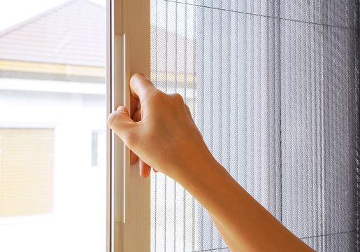 Woman hand hold retractable pleated insect screen holder to open or close the window ,selective focus on the hand