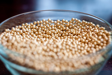 Close up of little golden balls in a clear transparent bowl.