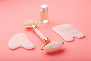 Gua sha massage tool made of natural pink Quartz-roller, jade stone and oil, on a pink background for face and body care. Part of traditional Chinese medicine