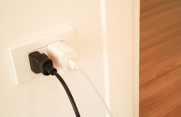 black and white plug of electrical appliance or device is plugging in the electric socket on white...