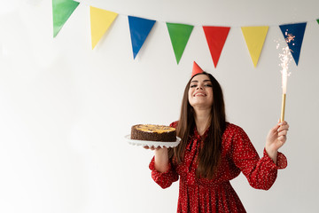 Beautiful and stylish girl in a red dress. Holiday birthday. Tasty cake and bengal fountain in the...