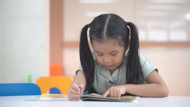 asian child cute or kid girl happy reading story book or student enjoy for learn to tale read with education on colorful chair and table in library classroom at nursery preschool and kindergarten 4K