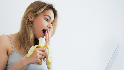 Beautiful funny young woman using laptop device in bed. Eating healthy fruits at home in bed. Handsome influencer lifestyle. 