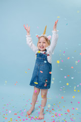 Happy little girl in unicorn head band clapping her hands over blue background