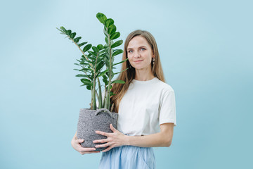 Happy woman standing with a plant in a wicker pot, she's holding in her hands