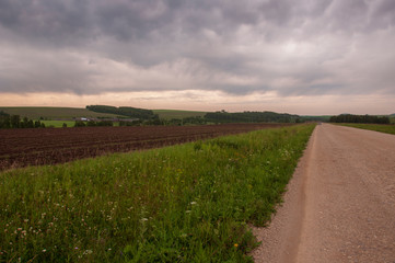 Big autumn field with trees far away and clouds in the blue sky. Asphalt road. Travelling 