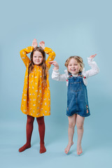 Two little girls making easter bunny ears gesture with hands over blue