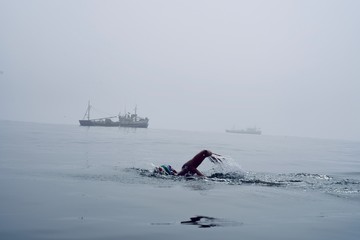 open water swimmer in flat water, swimming in misty conditions with fishing boat in the background