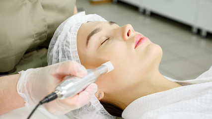 Obraz na płótnie Canvas lady in green coat makes microdermabrasion procedure on face of beauty salon patient lying on white couch