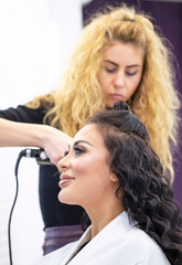 Fototapeta premium The hairdresser curls the hair of a young smiling girl