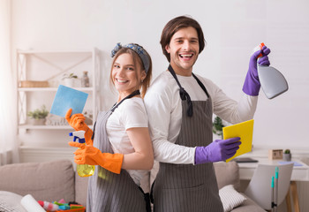 Cleaning service professionals. Joyful millennial couple holding detergent sprays and rags