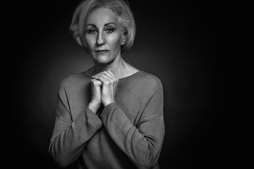 Classic black-and-white dramatic portrait of elderly blonde woman in Studio on black background