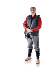Fototapeta premium A man with a gray beard, in a cap, a black vest, with a bag and a gun in his hands isolated on a white background. The man is on the hunt.