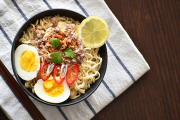 Instant noodles with minced pork, egg, lemon grass, chilli and lemon in a black bowl with copy space on the right side. Selective focus. Thai style Tom Yum noodles. 