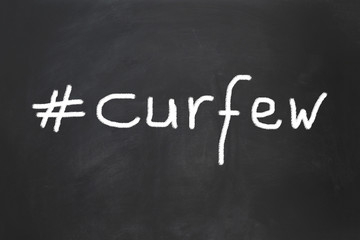 hashtag curfew as handwritten text on chalkboard - social distancing measure to control infection during corona virus pandemic