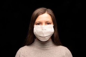 a woman's face in a white medical mask on a black background. gaze directed at the camera , close-up portrait. beautiful eye