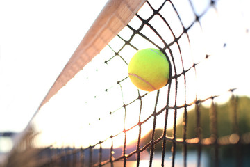 Bright greenish yellow tennis ball hitting the net.