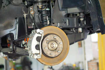 Fototapeta premium car brake part at garage,car brake disc without wheels.Disk brake and car disk brake system service concept - Car disk brake pad replacement service by hand of mechanic man in car garage.Close up.