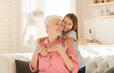 Family bonding. Lovely little girl happily emracing her grandma in light living room