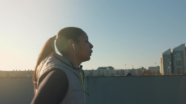 portrait of a young dark skin woman while she's running in a city during winter's sunset